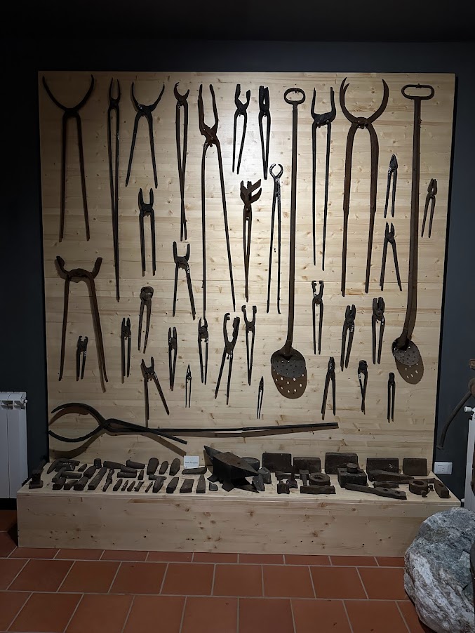 Fotografia di una parete con esposti diversi strumenti per l'agricoltura, tra qui quelli dedicati al maniscalco