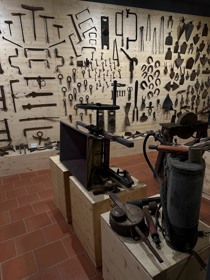 Fotografia di una parete con esposti diversi strumenti da lavoro come seghe, ferri di cavallo, martelli